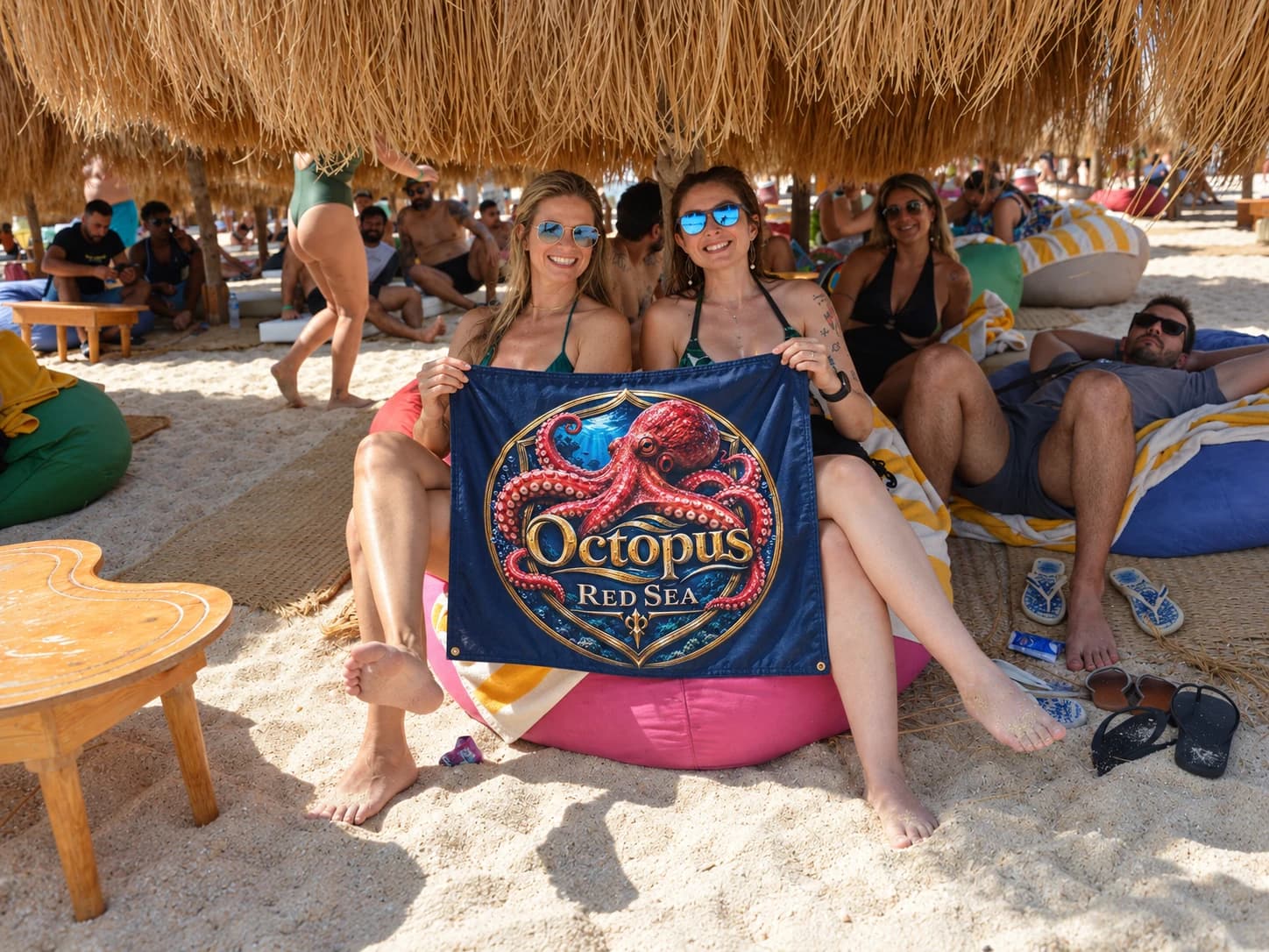 Travelers sitting beneath a shaded beach shelter holding an Octopus Red Sea banner