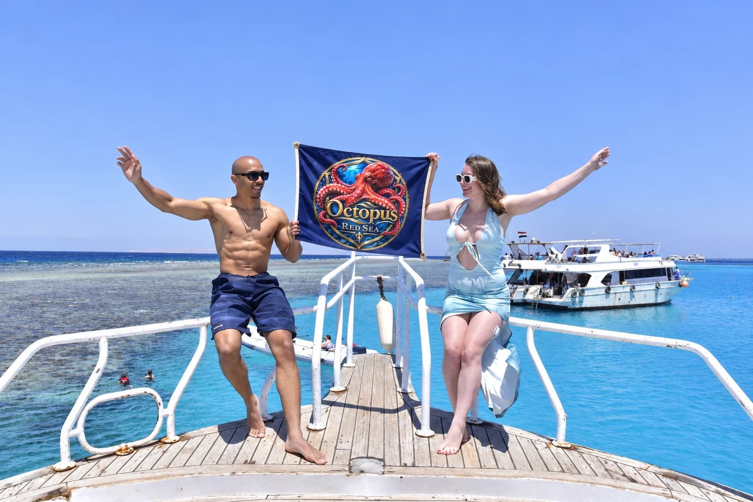 Couple posing above the clear Red Sea holding an Octopus Red Sea banner
